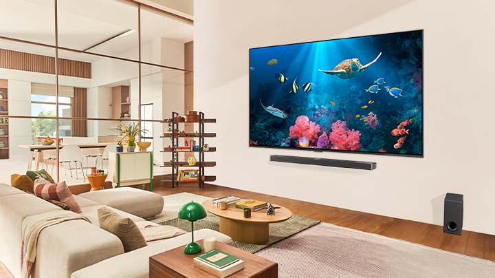 A family in a living room with an ultra big LG TV mounted on the wall, with an ocean scene including coral and a turtle on the screen.