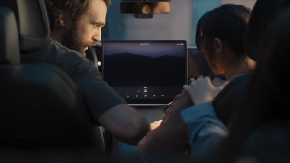 Inside a car with two people sitting, the LG AI logo is glowing on the screen.