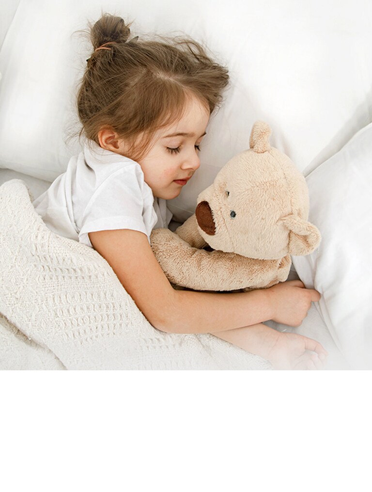 A little girl is lying in bed with a doll in her arms