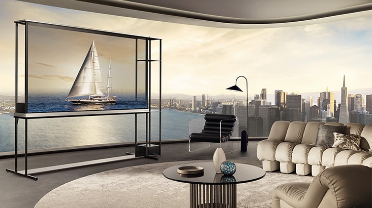 LG OLED T4 en un ático. La ventana mira hacia el perfil de la ciudad y el océano. El LG OLED T4 está en modo transparente mostrando una imagen de un yate. Debido a la posición del televisor y a la transparencia de la pantalla, parece que el yate está flotando en el océano.