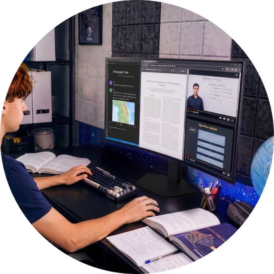 Un estudiante sentado en un escritorio estudia mientras consulta un trabajo de investigación y clases en línea en un monitor panorámico de gran tamaño.