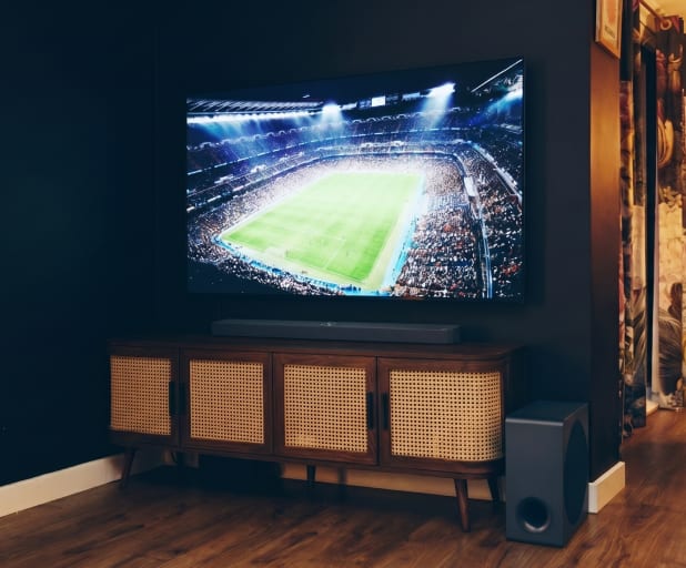 Primer plano de una barra de sonido debajo de un televisor sobre un mueble de madera.