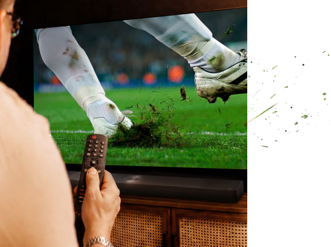 Un primer plano de las piernas inferiores de un futbolista mientras golpea el balón en un campo de hierba, con tierra y césped levantándose por el impacto.