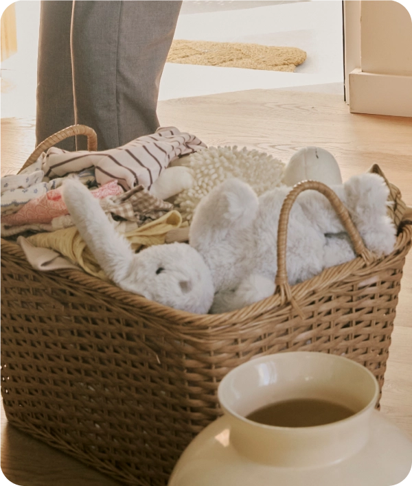 Un gran cesto de mimbre lleno de ropa y peluches sobre un suelo de madera.