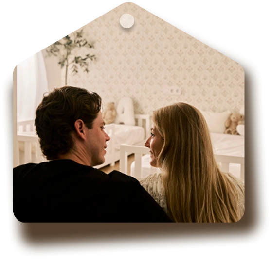 Una pareja vista de espaldas, mirándose con cariño en una habitación de bebé decorada en tonos suaves.