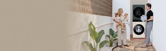 Una familia con gemelos pequeños de pie en un pasillo exterior de paredes blancas, junto a una lavadora y una secadora LG apiladas.
