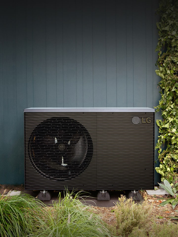 Bomba de calor aire-agua LG THERMA V R290 Monobloc, la unidad exterior de color negro se coloca en la pared verde exterior de la casa. 