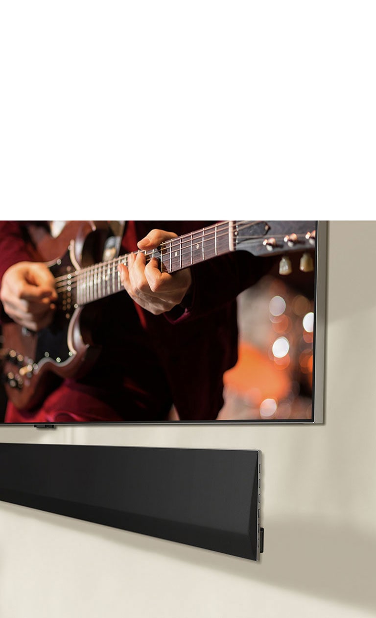 Una perspectiva en ángulo de la parte inferior de una barra de sonido LG y un televisor LG montada contra la pared.