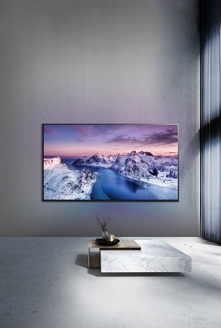 Un televisor UHD montado en la pared detrás de un tabe con ambientación de estilo zen.