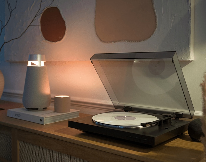 Altavoz LG XBOOM que emite una luz cálida junto a un tocadiscos sobre un mueble de madera.