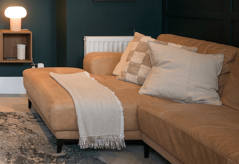Un sofá beige decorado con mullidos cojines y una manta con flecos.