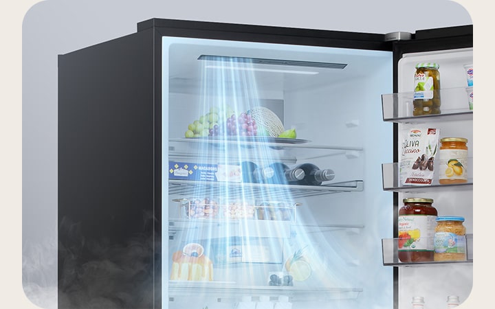 Abre el congelador inferior LG con aire azul claro fluyendo desde la rejilla de ventilación izquierda hacia las cestas de la puerta, con frutas, botellas y recipientes almacenados en su interior.    