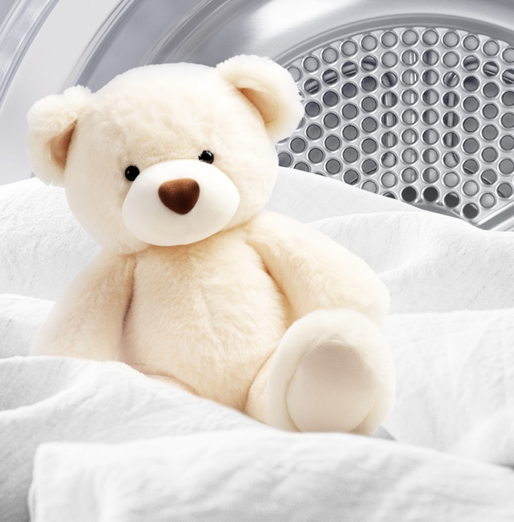 Imagen de un osito de peluche limpio y tela blanca dentro de un tambor de secadora.