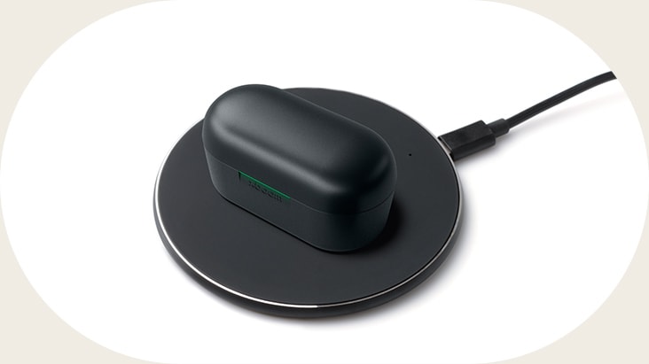 Un estuche negro de xboom Buds Plus se encuentra sobre una base de carga con la luz encendida, indicando que se está cargando.