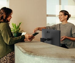 Una recepcionista amigable mostrándole a una mujer dónde firmar en una tablet digital.