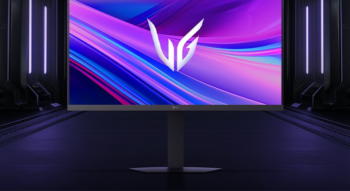 Vista frontal del monitor gaming LG UltraGear™ 27g440a sobre su base hexagonal, situado en un pasillo futurista iluminado con luces de neón; la pantalla muestra remolinos vívidos en tonos púrpura y rojo con el logotipo de UltraGear en el centro.