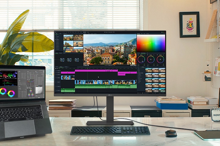 Un espacio de trabajo creativo con un monitor LG y un portátil conectado, ambos mostrando una interfaz de edición de vídeo con herramientas de corrección de color y una línea de tiempo.