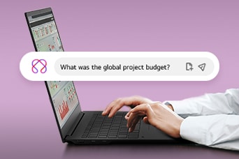 Esta imagen muestra unas manos escribiendo en un portátil, con una barra de búsqueda que muestra la pregunta: "¿Cuál fue el presupuesto global del proyecto?"