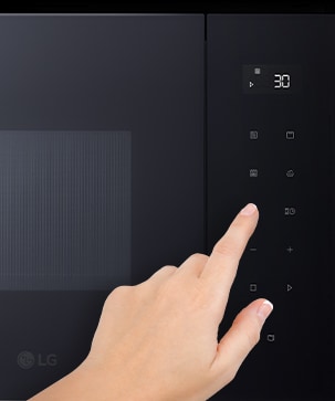 Panneau de contrôle du micro-ondes encastrable et doigt qui touche la commande.