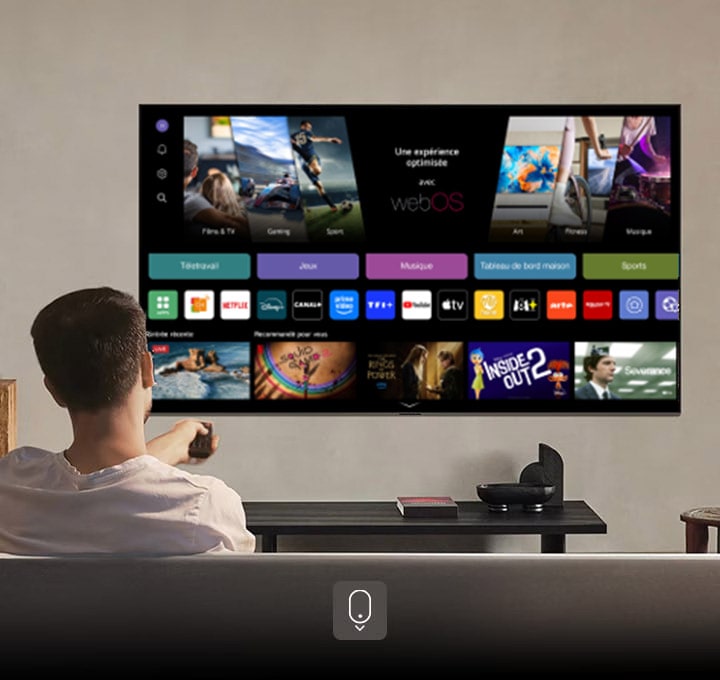 Une personne sur le canapé tenant une télécommande. LG AI TV sur le mur avec LG webOS à l’écran.