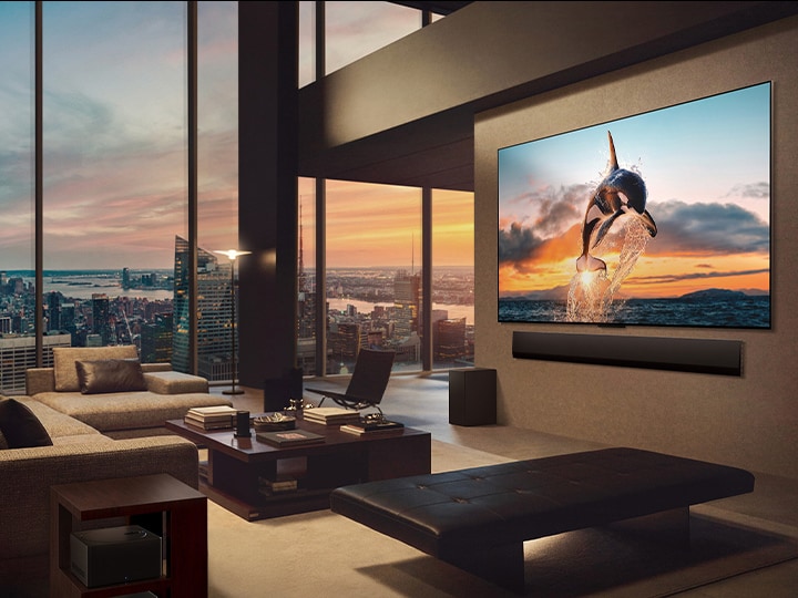 Un salon spacieux avec vue sur la ville. La LG OLED TV est fixée au mur avec une LG Soundbar. Le One Wall Design de la TV permet une installation murale encastrée pour bien se fondre dans l’espace. Le boîtier Zero Connect est visible, mais dissimulé.