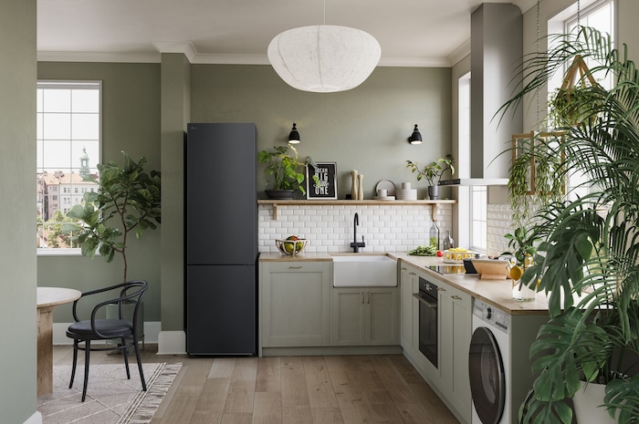 Réfrigérateur-congélateur LG GBV22NCCEP Noir Mat (203 cm de haut), intégré élégamment dans une cuisine moderne vert olive avec parquet et plantes d'intérieur.
