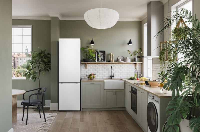 Réfrigérateur-congélateur LG GBV3200DSW Blanc (203 cm de haut), intégré élégamment dans une cuisine moderne vert olive avec parquet et plantes d'intérieur.