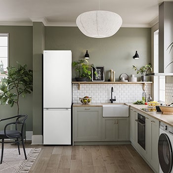 Réfrigérateur-congélateur LG GBV3200DSW Blanc (203 cm de haut), intégré élégamment dans une cuisine moderne vert olive avec parquet et plantes d'intérieur.