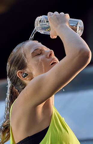  Une femme se passe de l'eau sur le visage avec TF8 sur l'oreille.