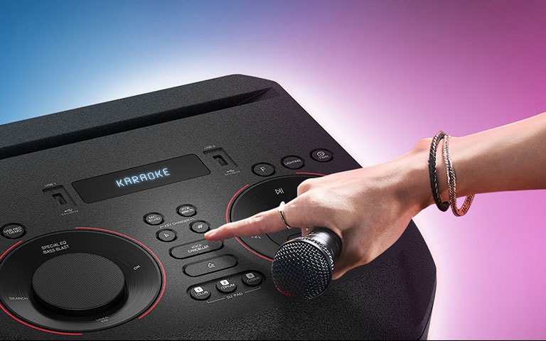 Une main tenant un micro appuie sur le bouton Voice canceller sur le dessus de l’enceinte LG XBOOM.