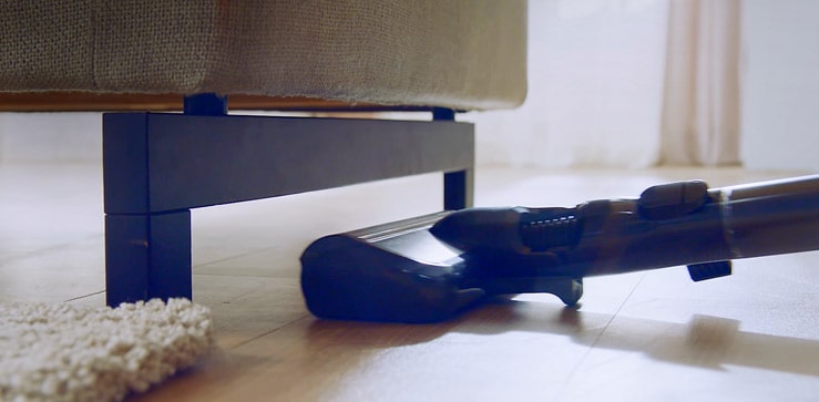 A woman's hand is seen comfortably gripping the handle of the vacuum as she cleans the living room.