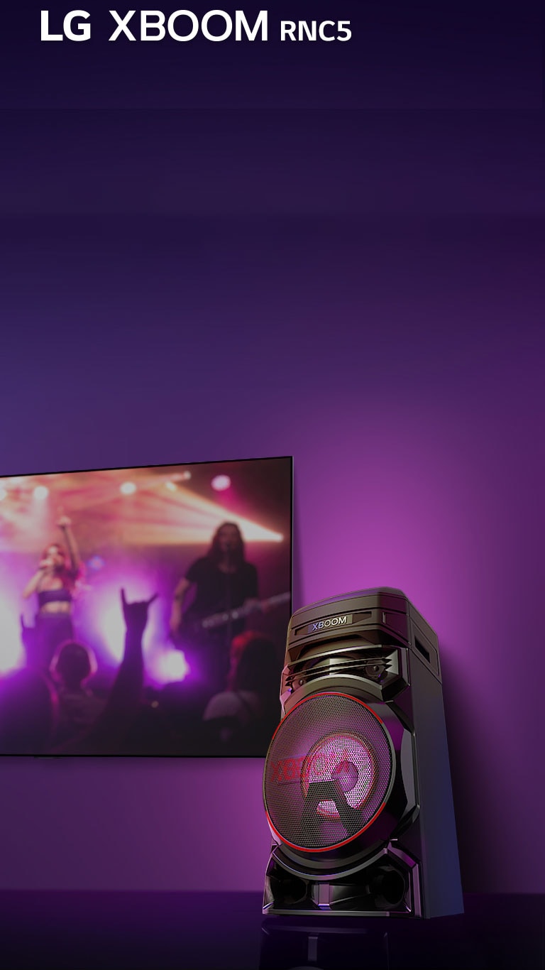 Vue en contreplongée du côté droit de l’enceinte LG XBOOM RNC5 sur fond violet.  L’éclairage du XBOOM est également violet. Et un écran de télévision diffuse un concert.