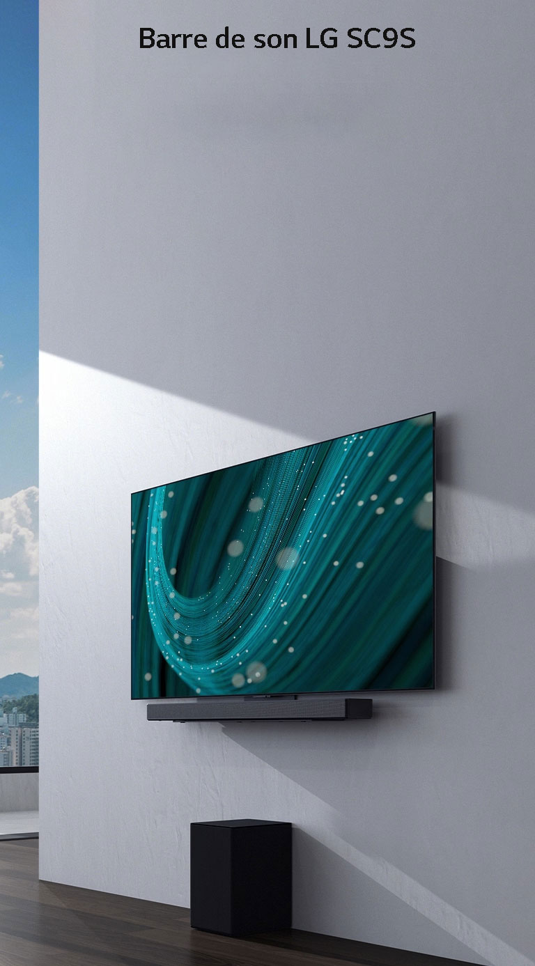 Un téléviseur et la barre de son LG SC9S sont accrochés sur un mur. En dessous, un caisson de basses noir en placé sur le sol. À gauche, une vue de la ville avec un ciel bleu se dessine derrière une fenêtre.