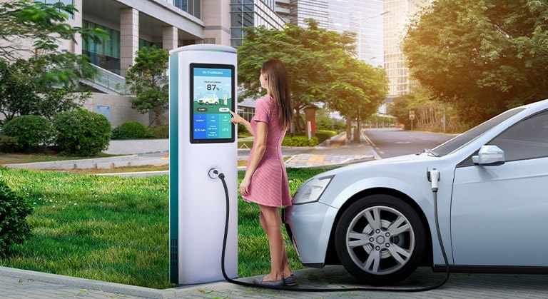 Une femme recharge une voiture en touchant l’écran tactile installé sur un chargeur de voiture électrique.
