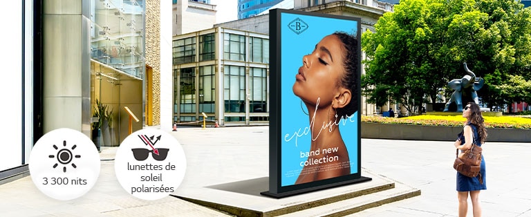 Un grand écran est installé à un arrêt de bus. Une femme y observe une publicité d’une qualité éclatante.