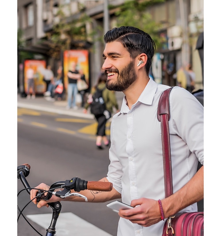 Un homme pousse son vélo en ville tout en portant ses écouteurs.