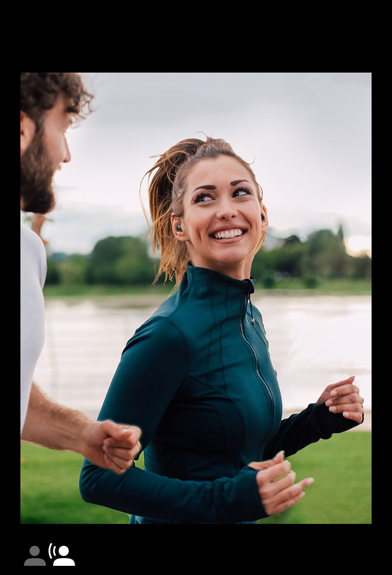 Un homme et une femme courent dans un parc avec des écouteurs TONE Free fit aux oreilles.