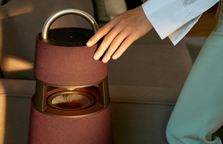 Image d’une femme touchant l’extérieur d’une enceinte XBOOM 360 de couleur bordeaux.