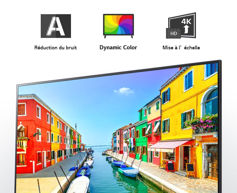 Un écran de téléviseur affiche une ville portuaire dans laquelle les immeubles sont peints en plusieurs couleurs et de petits bateaux sont ancrés le long d’un quai long et étroit.