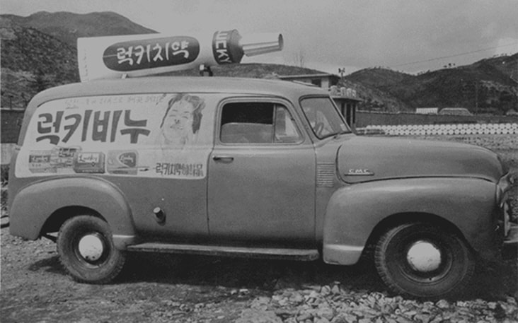 Vintage delivery truck with a large Lucky Toothpaste model on top and Lucky Cream ad painted on the side