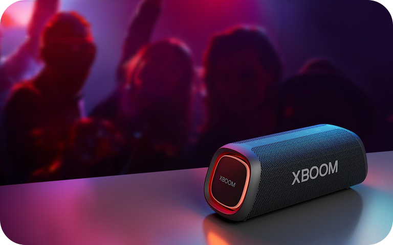 LG XBOOM Go XG5QBK portable Bluetooth speaker on a table with party lights and lively atmosphere in the background