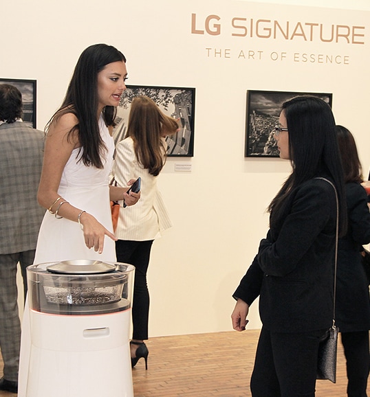 people are staring at photographs of lg signature products and a curator is explaning about lg signature air purifier at launching event in colombia