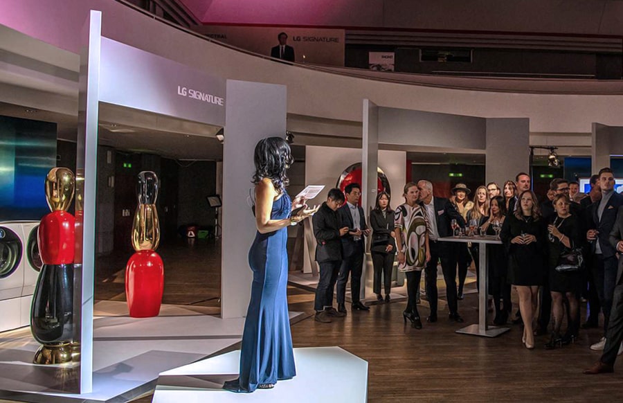 many people are standing and staring the main stage and one woman is talking to everyone in front of lg signature oled tv at artweek in germany