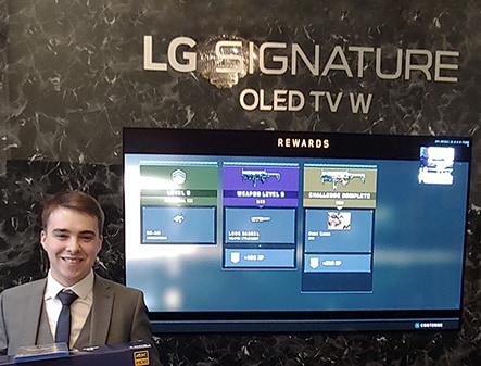 a man is standing and holding giveaway ps4 in frong of lg signature oled tv whis is hung on the right in the middle of the wall
