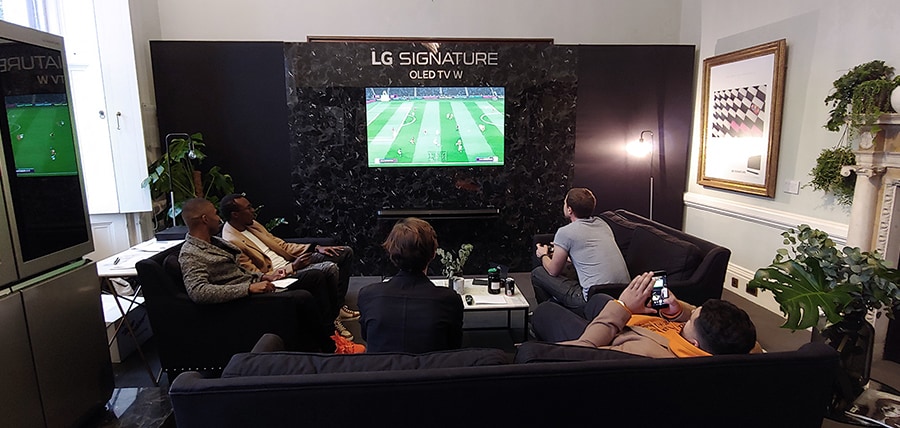 several people are sitting on the couch and looking on the lg signature oled tv whis is hung oh the right in the middle of the wall