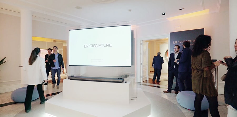 lg signature oled tv w is hung on the glass wall in the right middle at artweek in spain and some people are looking around exhibition