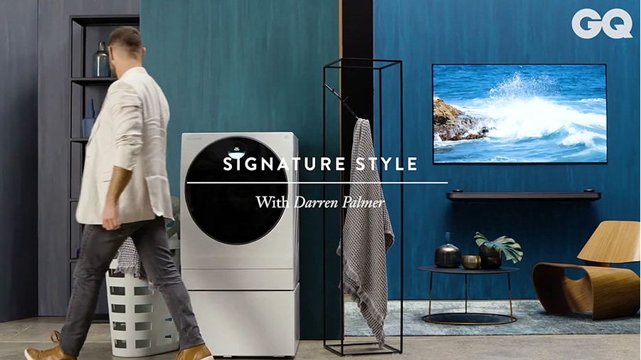 darren palmer is walking by lg signature washing machine which is laid in the overall blue colored living room with lg signature oled tv w on the right side