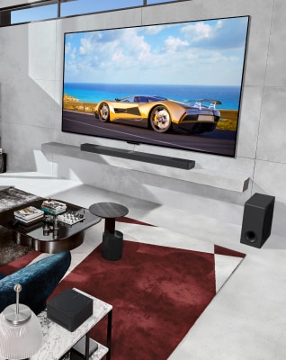 A man and a dog are sitting on a blue sofa in a stylish living room with a view of the sea, watching a OLED M TV mounted on the wall.