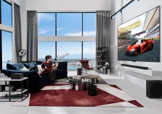 In a stylish living room overlooking the sea, a man is enjoying a car racing game on OLED M TV with zero connect box.