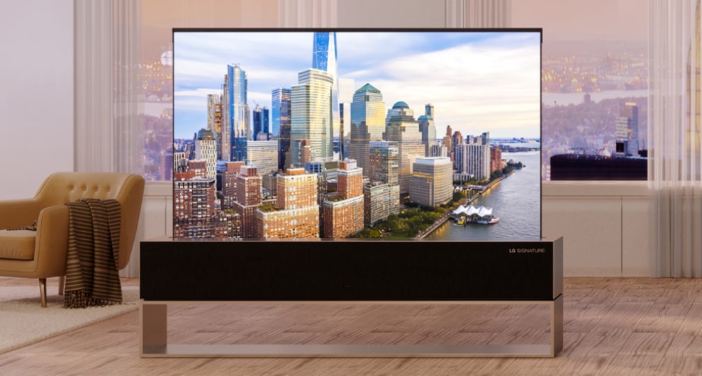 Ein Mann sitzt mit gekreuzten Beinen auf einem Liegestuhl und sein Körper zeigt zum rollbaren OLED-Fernseher LG SIGNATURE.